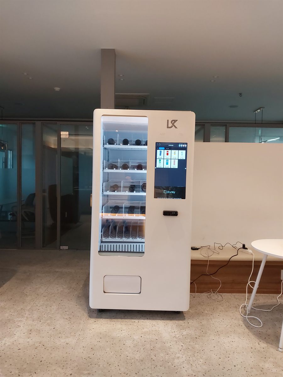 사무실 라운지 기둥 옆에 설치한 흰색 냉장 음료·간식 자판기와 터치 화면